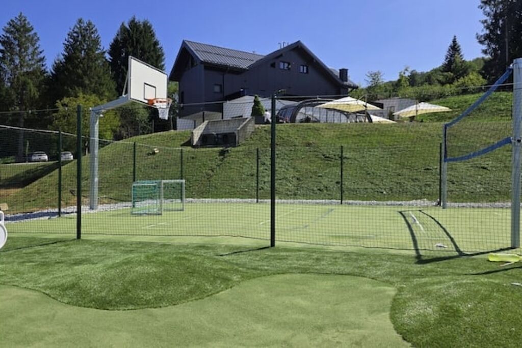 Un campo da basket con canestro e rete, e una casa sullo sfondo.