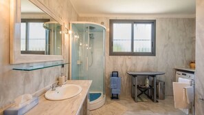 A modern bathroom with a glass-enclosed shower, a marble sink, a mirror, and a window. - Villa Arkè (Capilungo)