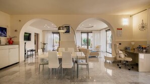 Eine moderne Küche mit weißen Schränken, ein Essbereich mit Glastisch und Stühlen sowie eine Wohnbereich mit Sofa und Sesseln.
