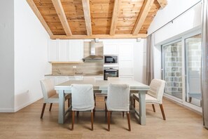 Een moderne keuken met witte kasten, een houten plafond en een eethoek met rieten stoelen.