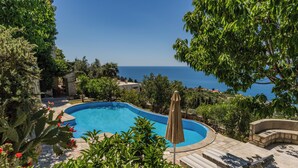 A swimming pool with a curved edge, surrounded by lush greenery and a view of the sea. - Castello degli Aranci Eco Resort (Krstac)