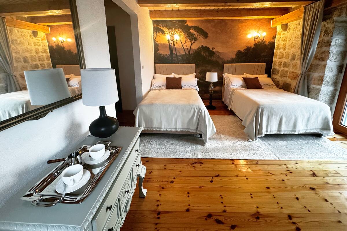 Une chambre d’hôtel avec deux lits, une commode sur laquelle est posée une assiette contenant de la vaisselle blanche, un miroir et une fresque représentant des arbres.