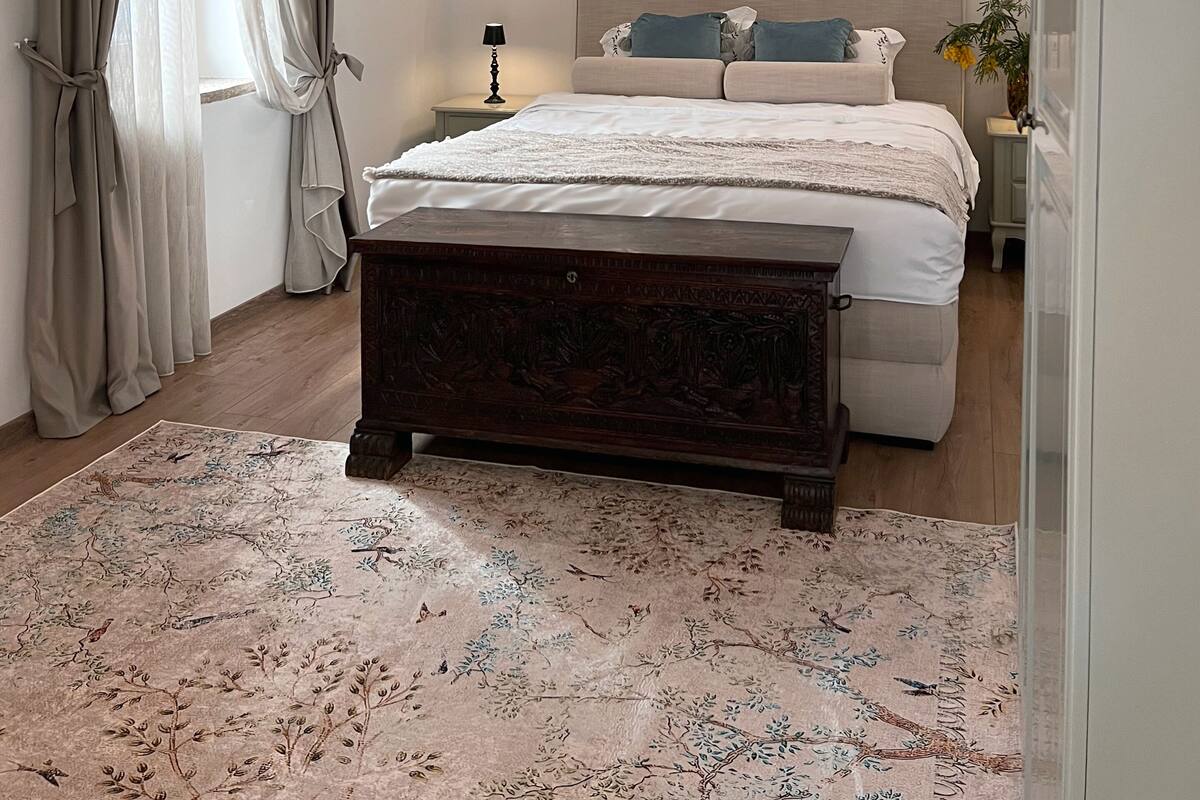 Une chambre à coucher comprenant un lit, une table de chevet, une lampe, un luminaire fixé au mur et une fenêtre avec des rideaux.