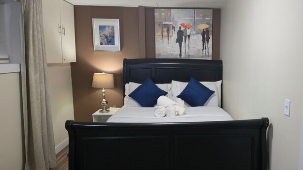 A neatly made bed with white and blue bedding, a bedside lamp, and a framed picture on the wall. - Cozy 2-Bedroom Suite | Private Access | Near Everything (Edmonton)