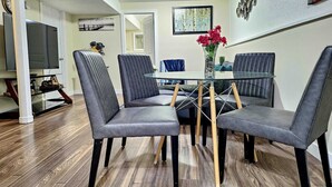 A dining area with a glass table surrounded by four upholstered chairs with wooden legs. - Cozy 2-Bedroom Suite | Private Access | Near Everything (Edmonton)
