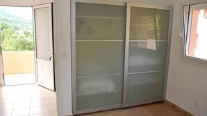 Quarto com porta de vidro deslizante para uma varanda, piso de azulejos e janela com vista para vegetação.