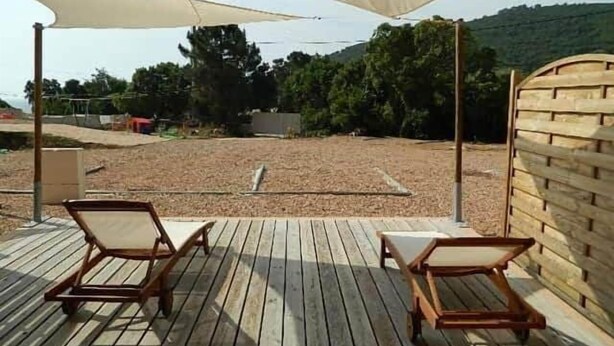 Een houten terras met twee ligstoelen onder een grote zonwering.
