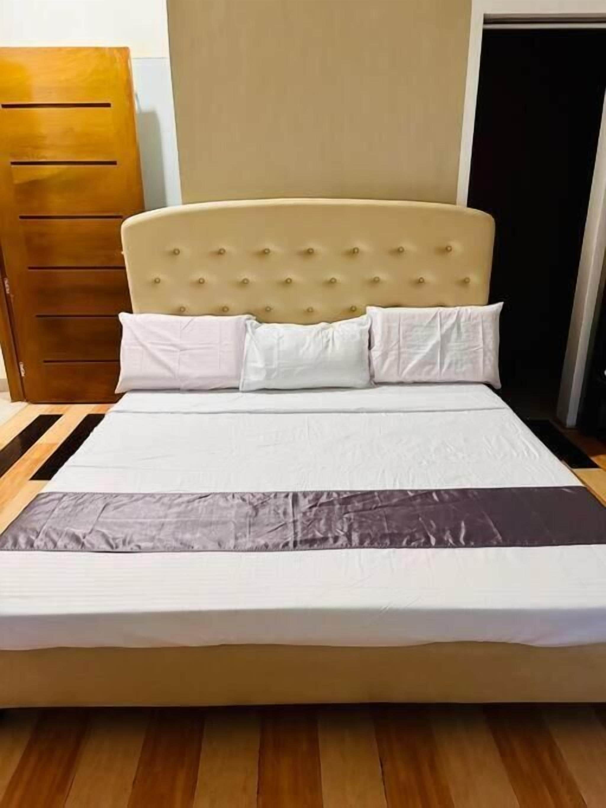 Un lit avec une tête de lit capitonnée, du linge de lit blanc et un plancher en bois.