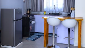 A compact kitchen with a refrigerator, oven, and a small bar area with two stools.