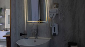 A bathroom with a marble wall, a sink, a mirror, and a hairdryer plugged in.