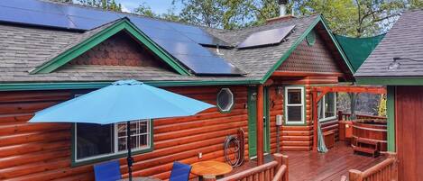 Una cabaña de troncos con terraza, paneles solares y una mesa con sillas.