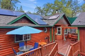 Eine Blockhütte mit einer Terrasse, Solaranlagen und einem Tisch mit Stühlen.