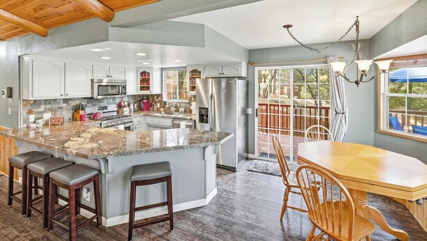 A spacious kitchen with a large island, bar stools, and a dining table with chairs. - Resort-Style Backyard with Cedar HOT TUB, Sauna, Firepit & Putting Green! PET FRIENDLY! 2 Split Ductless Air Conditioning Units!FREE EV Charger! (Big Bear City)