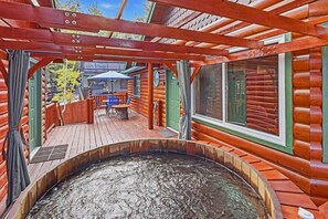 A wooden deck with a hot tub, a covered seating area, and a view of a cabin. - Cedar HOT TUB on Front Deck! Resort-Style Backyard w/Sauna, Firepit & Putting Green! PET FRIENDLY! Split Ductless A/C! FREE EV Charger! (Big Bear City)