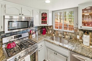 A kitchen with white cabinets, stainless steel appliances, granite countertops, and a window with a view of a wooden deck. - Cedar HOT TUB on Front Deck! Resort-Style Backyard w/Sauna, Firepit & Putting Green! PET FRIENDLY! Split Ductless A/C! FREE EV Charger! (Big Bear City)