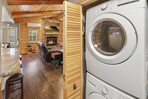 A laundry area with stacked washers and dryers, a fireplace, and a cozy seating area with a table and chairs. - Cedar HOT TUB on Front Deck! Resort-Style Backyard w/Sauna, Firepit & Putting Green! PET FRIENDLY! Split Ductless A/C! FREE EV Charger! (Big Bear City)