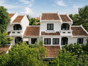 A white colonial-style building with multiple tiled roofs and large windows. - MUCA Hoian Co-living & Work Retreat (Hoi An)