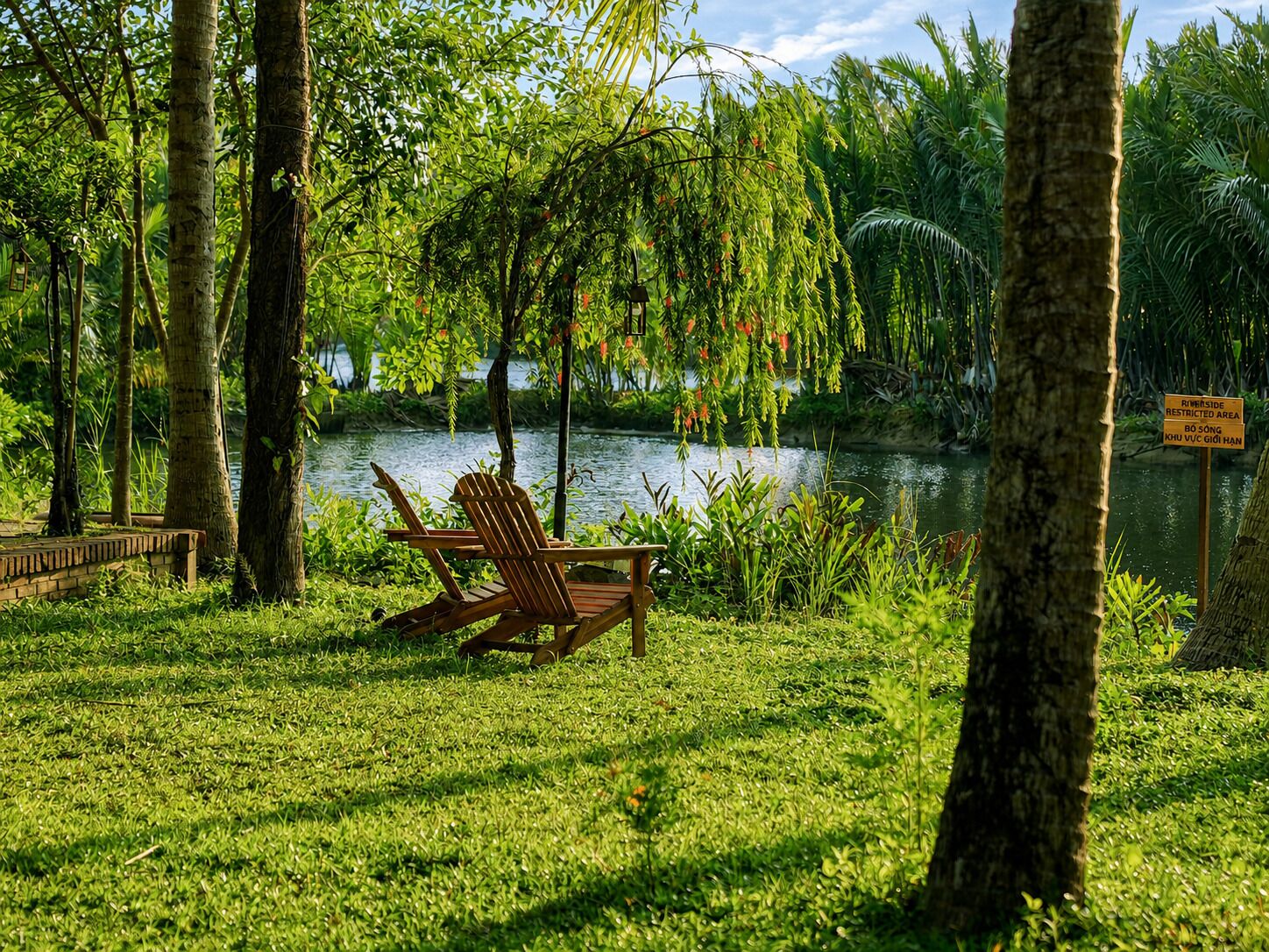 A serene lakeside setting with a wooden chair and a bench, surrounded by lush greenery and trees.