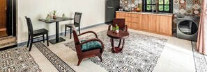 A room with a dining table, two chairs, a sofa, a small round table with a vase, and a kitchen area with a washing machine. - MUCA Hoian Co-living & Work Retreat (Hoi An)
