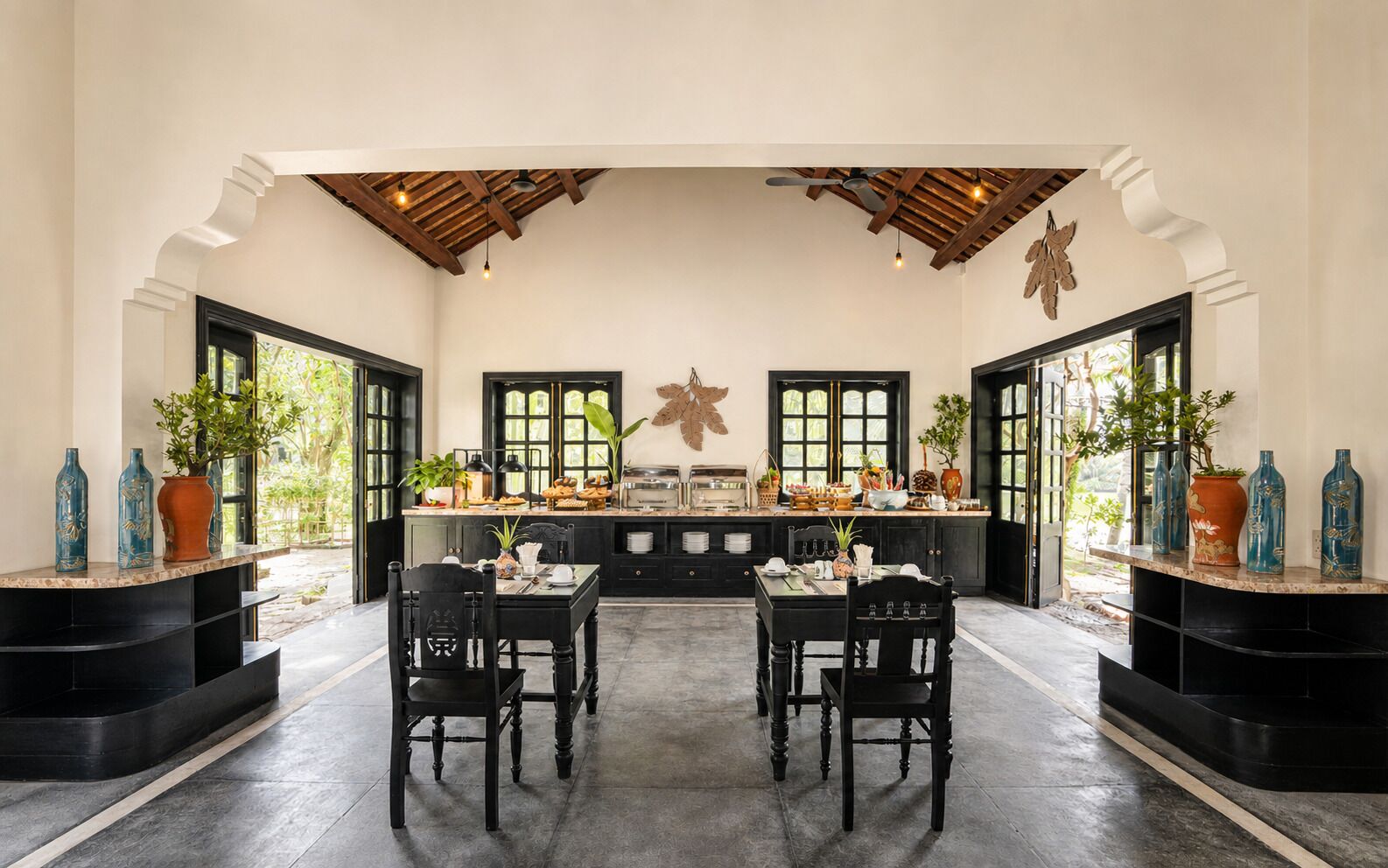 Un comedor con cocina al fondo, que cuenta con una isla central con asientos, sillas negras y una variedad de plantas y utensilios de cocina sobre la encimera.