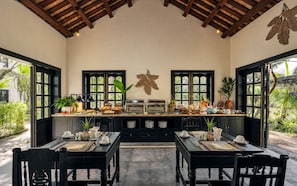 A dining area with a long counter, black chairs, and a ceiling with wooden beams. - MUCA Hoian Co-living & Work Retreat (Hoi An)