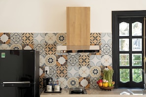 A kitchen with patterned tiles, a black refrigerator, a wooden range hood, and a window with a view. - MUCA Hoian Co-living & Work Retreat (Hoi An)
