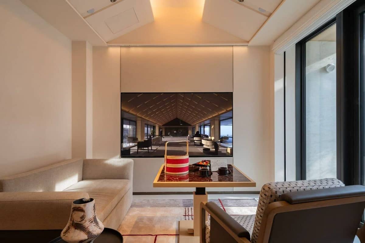 Une chambre d’hôtel moderne dotée d’une grande fenêtre, d’un canapé, d’une table basse et offrant une vue sur l’intérieur de l’hôtel.