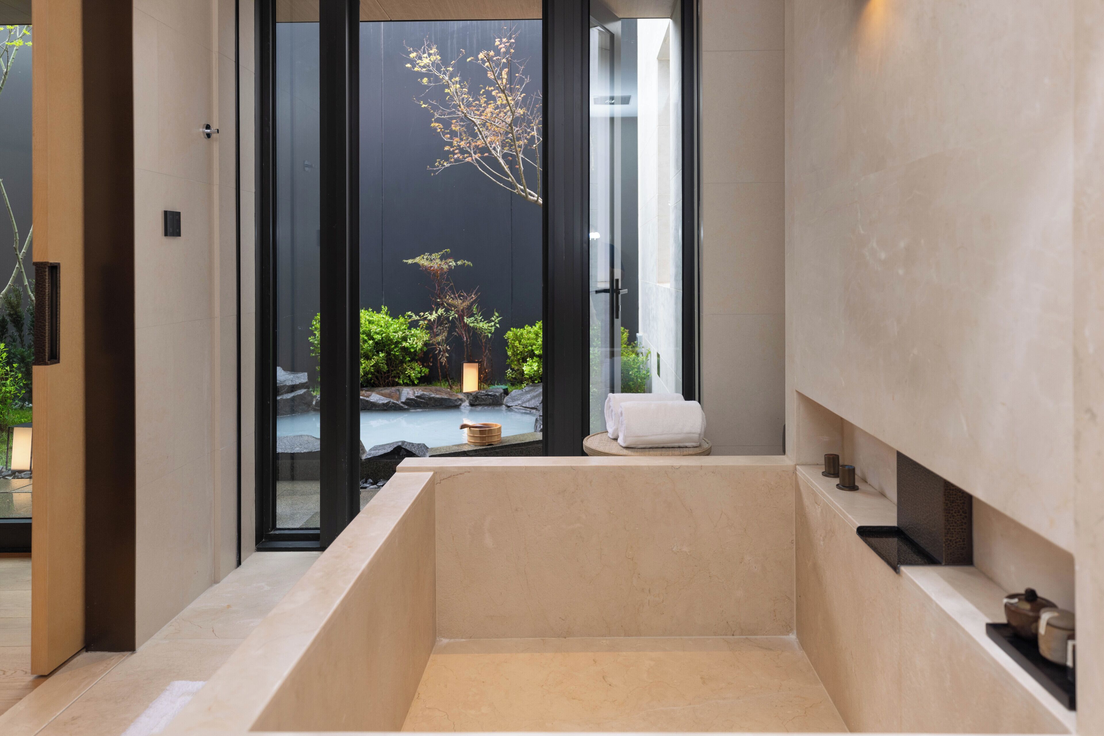 Un baño moderno con una bañera grande, una puerta de vidrio que da a un jardín y una toalla sobre el borde.