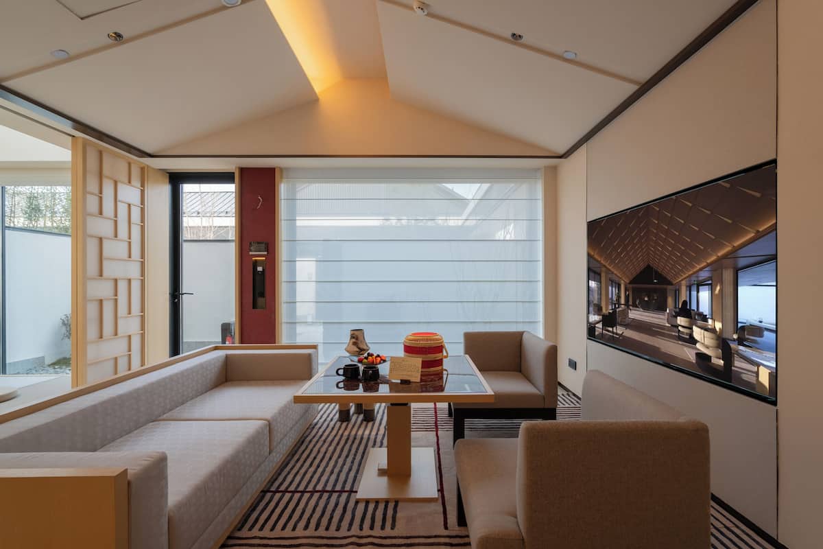 Une chambre d’hôtel moderne avec une table en verre, un coin salon et de grandes fenêtres.