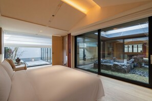 Un dormitorio moderno con una cama grande, un muro de cristal y vistas a un patio exterior.