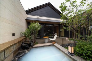 Una casa moderna con un muro de piedra, una pequeña piscina, una silla blanca y una mesa de madera.
