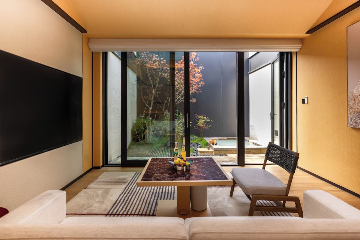 Un salon moderne avec un canapé, une table sur laquelle on voit des fruits, et une vue à travers de grandes portes vitrées.