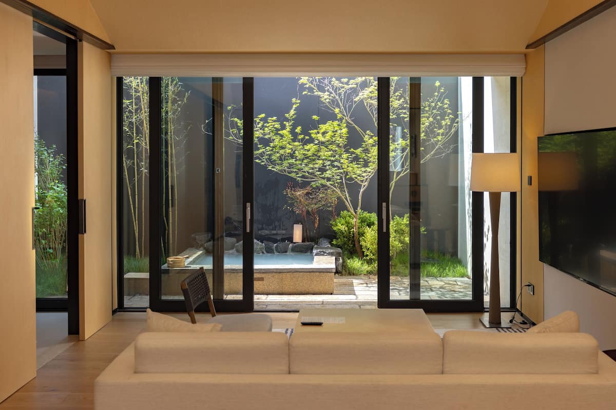 Un salon moderne avec un canapé, un téléviseur et une porte-fenêtre coulissante donnant sur un jardin.