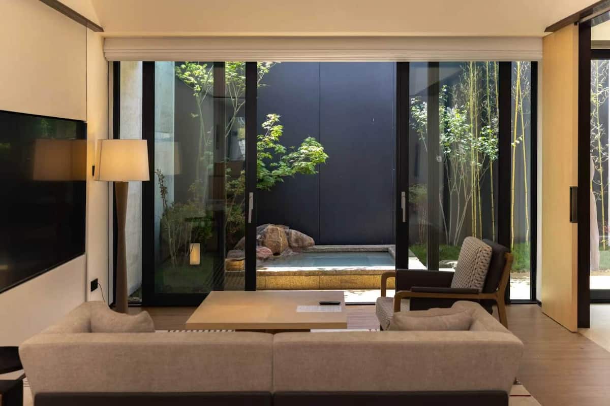 Un salon moderne avec un canapé, une table basse et un téléviseur. Une porte-fenêtre coulissante donne accès à un jardin agrémenté de plantes et d’une petite piscine.