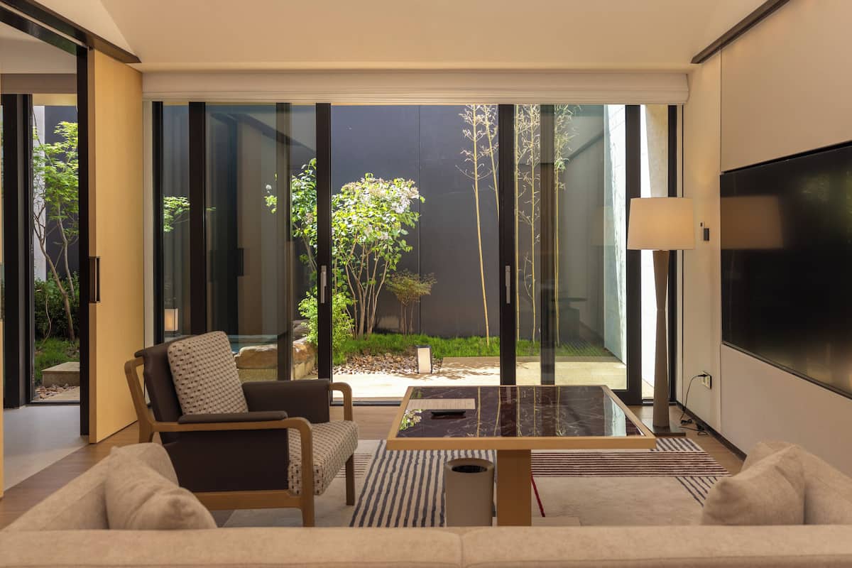 Un salon moderne avec un canapé, un fauteuil et une table basse, de grandes fenêtres et un téléviseur à écran plat.