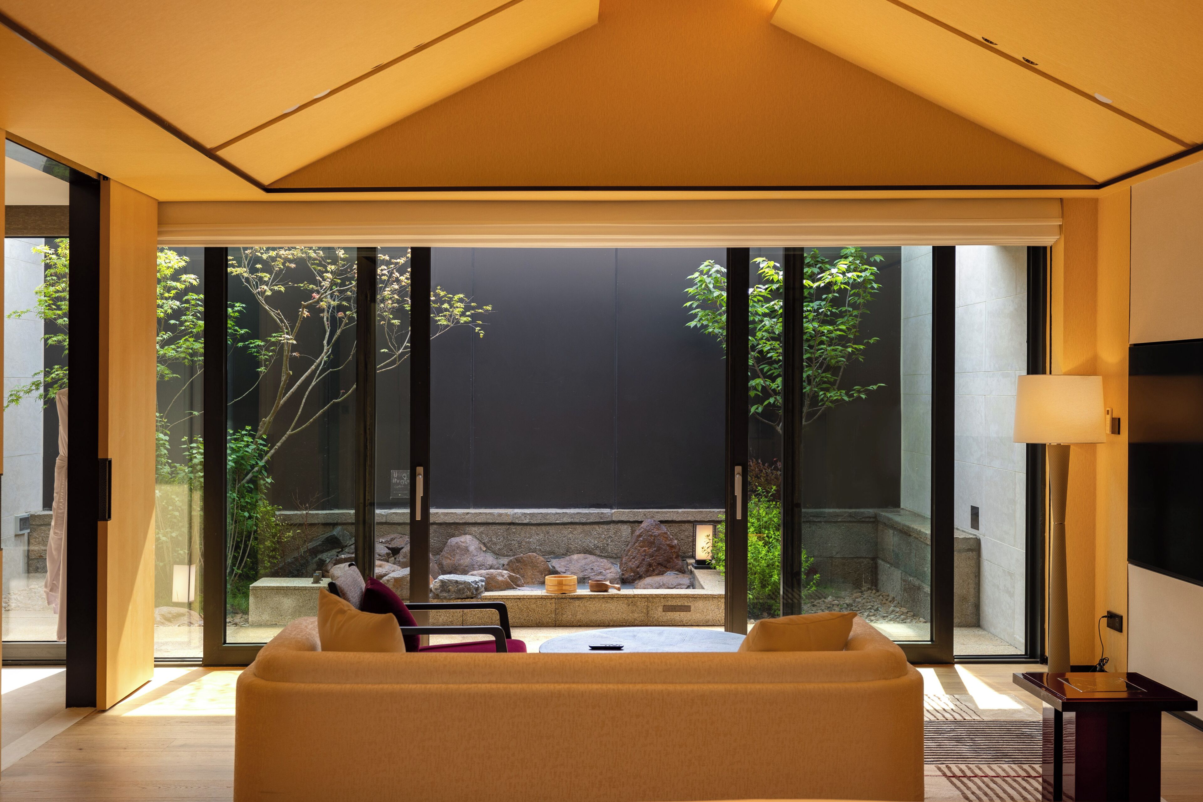 Un interno moderno con un divano, un tavolo e vista su un giardino tramite ampie vetrate.