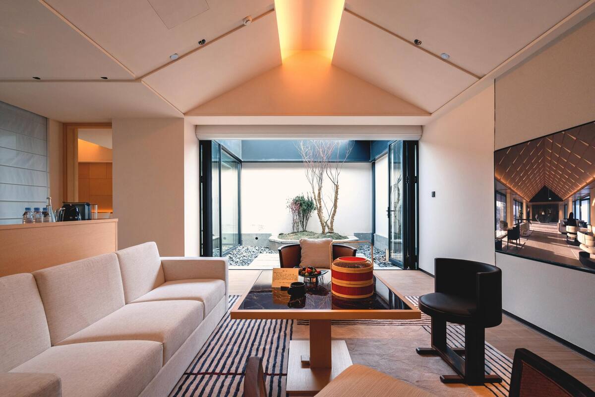 Un salon moderne avec un canapé, une table basse et une table  à manger. De grandes fenêtres offrent une vue sur un jardin.