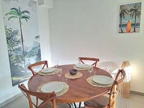 A round wooden dining table with six chairs, each with a woven placemat and a white plate. A woven bowl is placed in the center. - Pleasant T3 just a few minutes walk from the lagoon! (LA SALINE LES BAINS)