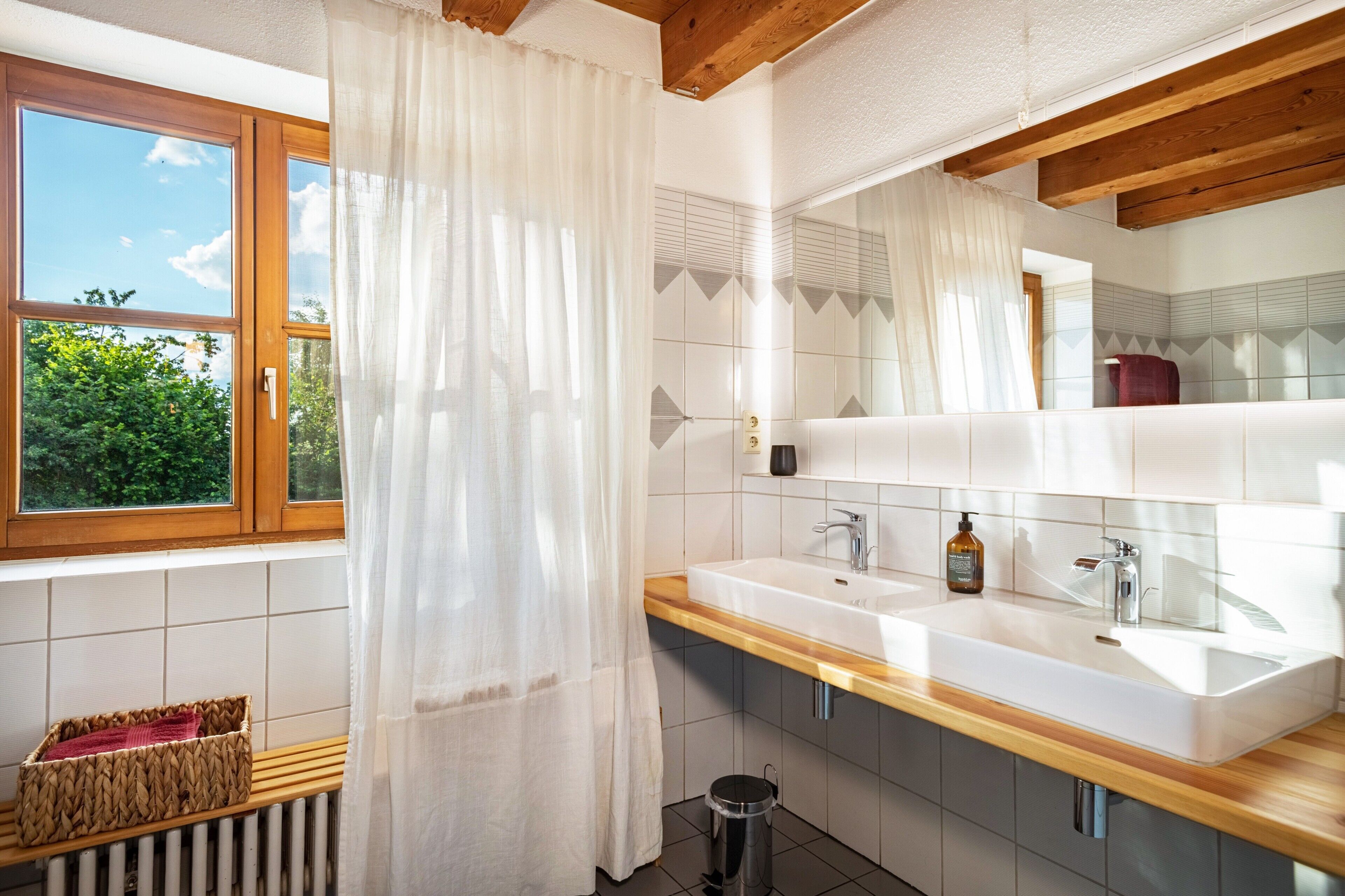 Ein Badezimmer mit Holzboden, einem großen Fenster mit Blick auf Grünfläche, einem weißen Waschbecken und einem Spiegel.