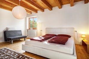 A bedroom with a bed, a sofa, a wooden ceiling, and a window.