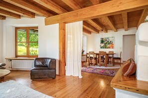 A spacious living area with a wooden ceiling, a leather sofa, a dining table with chairs, and a view through a large window. - Holiday Home “With Sun Terrace” with Balcony and Wi-Fi (Ostrach)