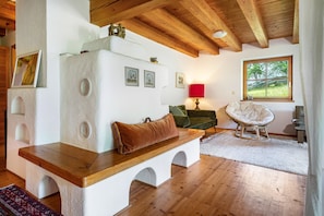 A cozy room with a wooden bench, a cushioned chair, a red lamp, and a window with a view of greenery. - Holiday Home “With Sun Terrace” with Balcony and Wi-Fi (Ostrach)