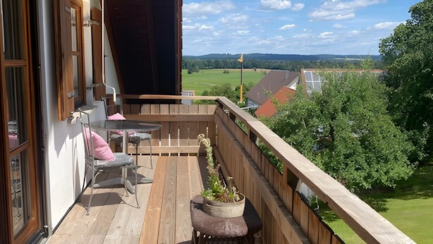 Eine Holzterrasse mit Gartenmöbeln, einem Blumentopf und Blick auf die Landschaft.