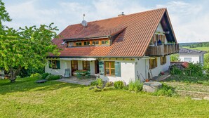 Ein zweistöckiges Haus mit geneigtem Dach, einem Balkon und einem Garten.