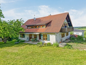 Ein zweistöckiges Haus mit geneigtem Dach, einem Balkon und einem Garten.