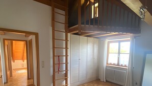 Ein Zimmer mit Holzboden, einem weißen Bett, einem Erker mit Aussicht und einem Heizkörper neben einem Fenster.