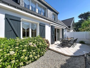 Kaksikerroksinen talo, jossa on patio, katettu ulko-oleskelualue ja suuri pensasaita.