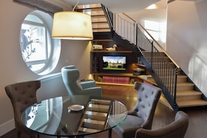 Una sala de estar moderna con una mesa de centro de vidrio, dos sillones tapizados, un televisor y una escalera con barandilla negra.