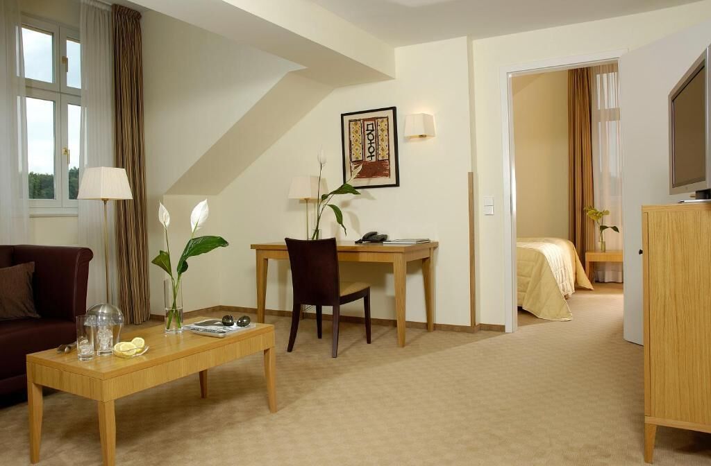 A hotel room with a sofa, a dining table with chairs, a desk, a bed, and a TV.