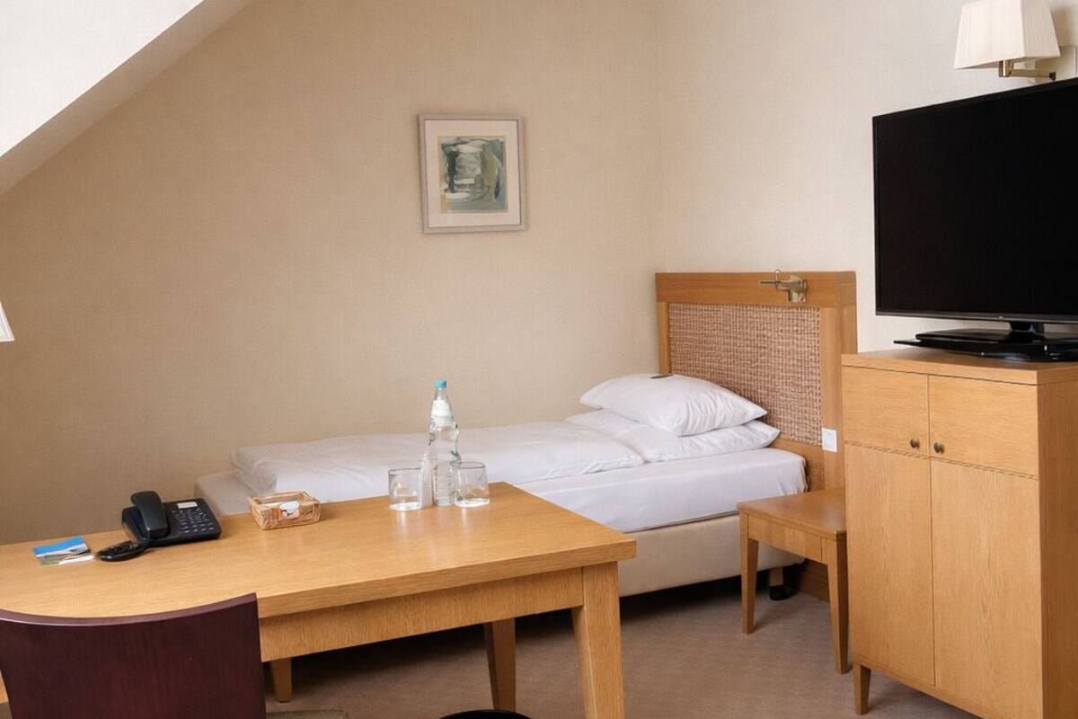 A hotel room with a bed, a desk with a phone, a television, and a chair.